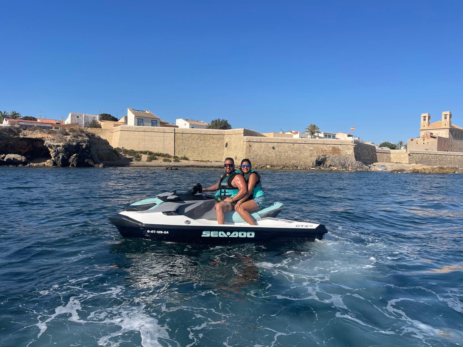 Pareja en moto de agua frente a la isla de Tabarca, con la fortaleza al fondo